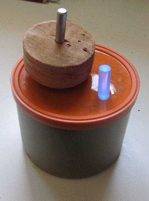 A can with a wooden knob and small cylinder emanating blue light above it